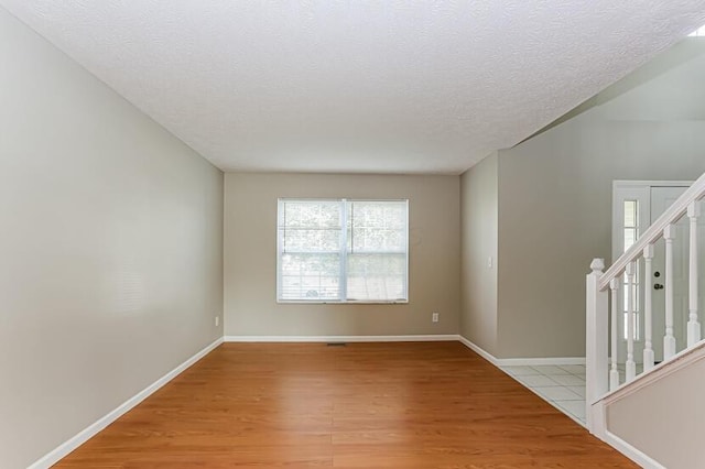 spare room with baseboards, light wood-style floors, stairs, and a textured ceiling