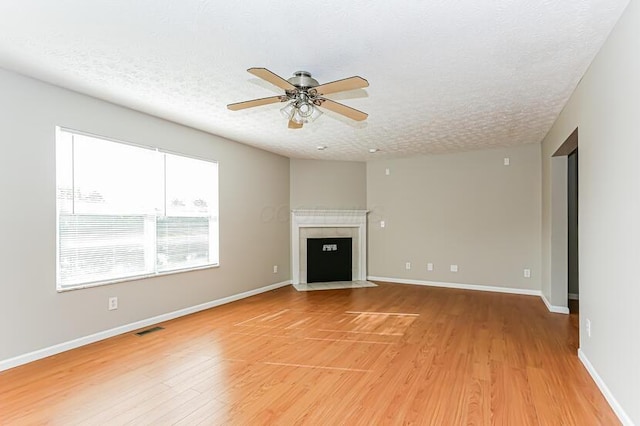 unfurnished living room with baseboards, visible vents, light wood-style flooring, a fireplace with flush hearth, and a textured ceiling