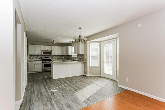 kitchen featuring tasteful backsplash, appliances with stainless steel finishes, dark wood-type flooring, and a peninsula