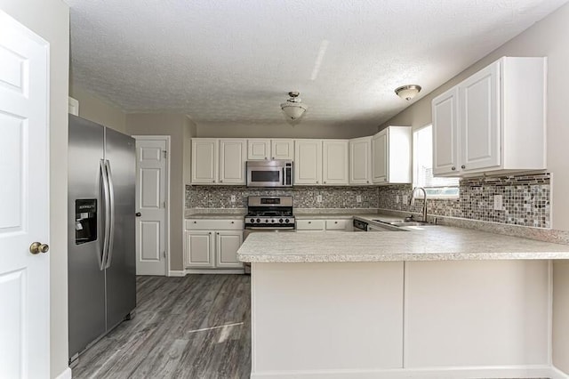 kitchen featuring a sink, dark wood finished floors, stainless steel appliances, a peninsula, and light countertops