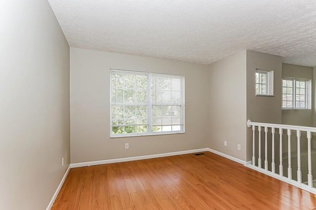 spare room featuring baseboards, light wood finished floors, and a textured ceiling