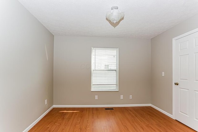 spare room featuring a textured ceiling, light wood-type flooring, and baseboards