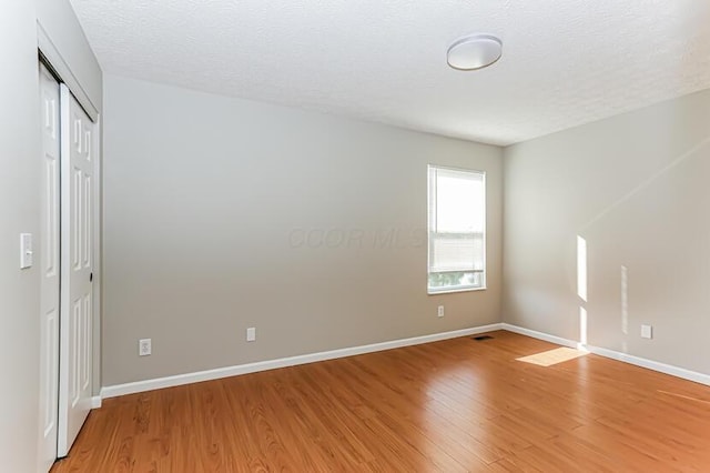 spare room featuring a textured ceiling, light wood-type flooring, and baseboards