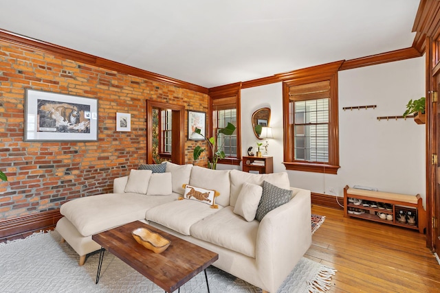 living room featuring brick wall, wood-type flooring, baseboards, and ornamental molding