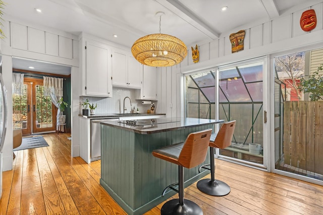 kitchen featuring beamed ceiling, light wood-style flooring, stainless steel dishwasher, dark countertops, and white cabinets