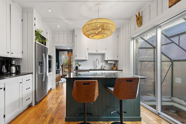 kitchen with light wood-style flooring, a sink, stainless steel appliances, white cabinetry, and a kitchen breakfast bar