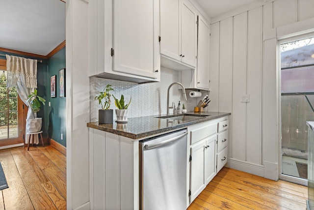 kitchen featuring light wood-type flooring, decorative backsplash, stainless steel dishwasher, white cabinets, and a sink