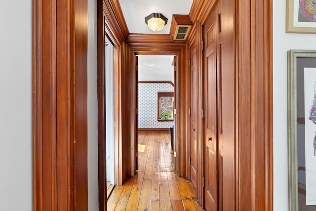 corridor featuring visible vents, wallpapered walls, crown molding, baseboards, and light wood-style flooring