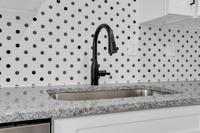 room details featuring light stone counters, white cabinetry, a sink, decorative backsplash, and dishwasher