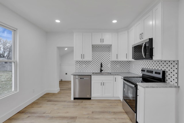 kitchen with light wood finished floors, backsplash, appliances with stainless steel finishes, white cabinetry, and a sink