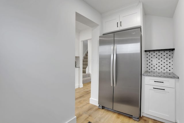 kitchen featuring light stone counters, white cabinetry, freestanding refrigerator, light wood finished floors, and baseboards