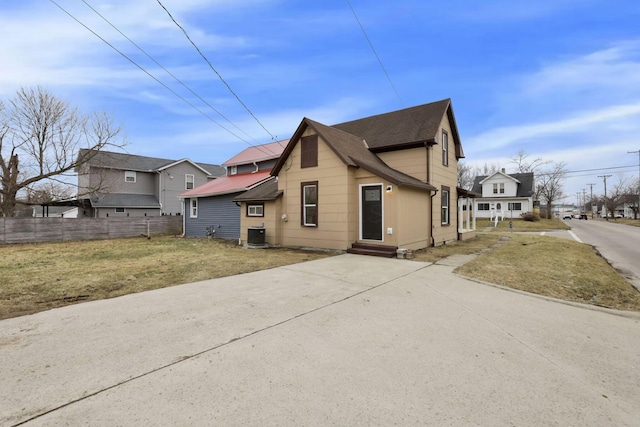 exterior space with central air condition unit, a front lawn, entry steps, fence, and roof with shingles