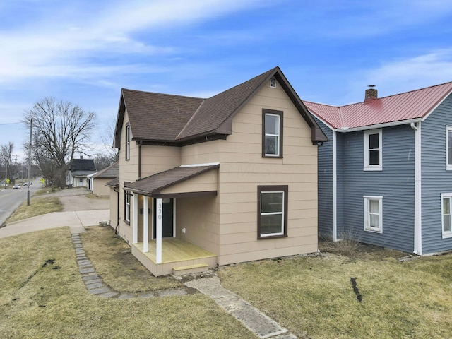 rear view of house featuring a porch, a yard, roof with shingles, metal roof, and a chimney