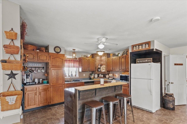 kitchen with brown cabinetry, freestanding refrigerator, ceiling fan, a sink, and light countertops