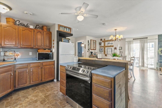 kitchen featuring stone finish flooring, brown cabinetry, freestanding refrigerator, and stainless steel range with electric cooktop