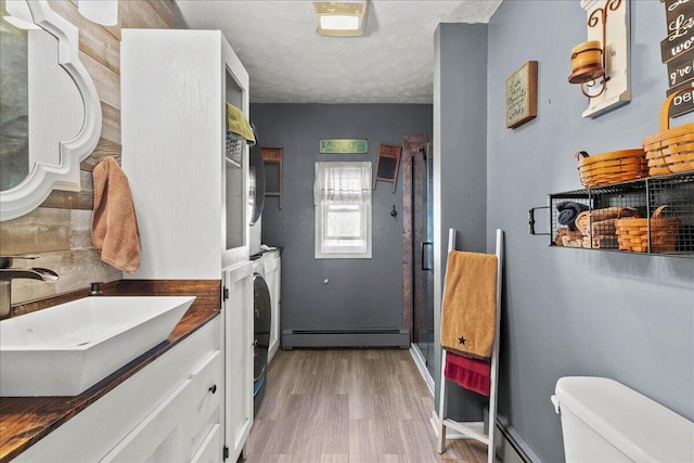 clothes washing area with stacked washer and dryer, a sink, a textured ceiling, a baseboard radiator, and laundry area