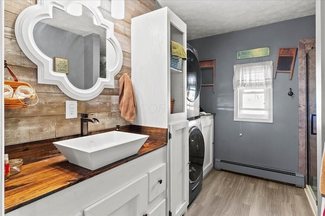 laundry area with stacked washing maching and dryer, laundry area, a sink, a baseboard heating unit, and light wood-type flooring