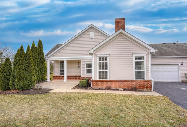 view of front of property featuring brick siding, driveway, a chimney, and a front lawn