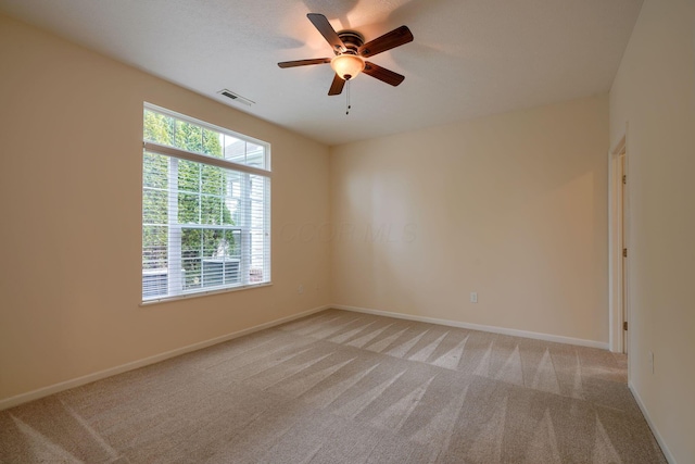 empty room featuring a ceiling fan, visible vents, light colored carpet, and baseboards