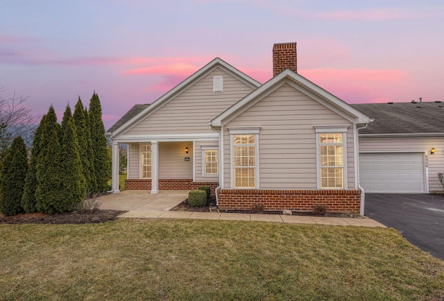 view of front of house with brick siding, an attached garage, aphalt driveway, and a yard