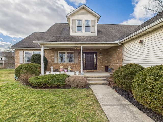 view of exterior entry with brick siding, a porch, a yard, and roof with shingles