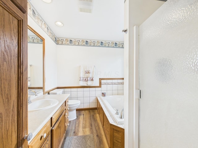 full bath with toilet, wood finished floors, tile walls, a bath, and vanity