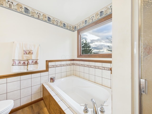 bathroom featuring a bath, toilet, and wood finished floors