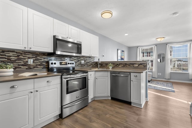 kitchen featuring white cabinets, appliances with stainless steel finishes, a peninsula, and a sink