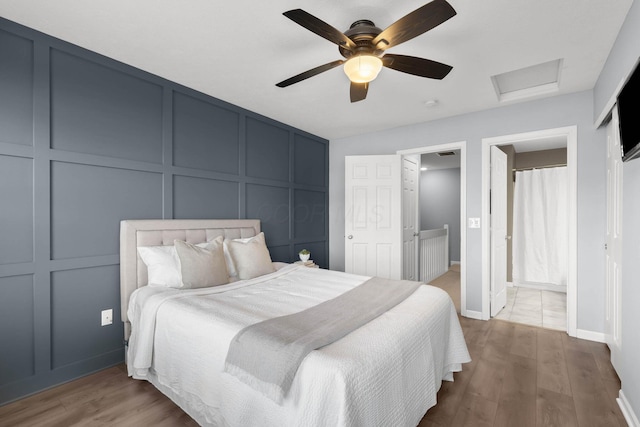 bedroom with a ceiling fan, wood finished floors, attic access, ensuite bathroom, and a decorative wall