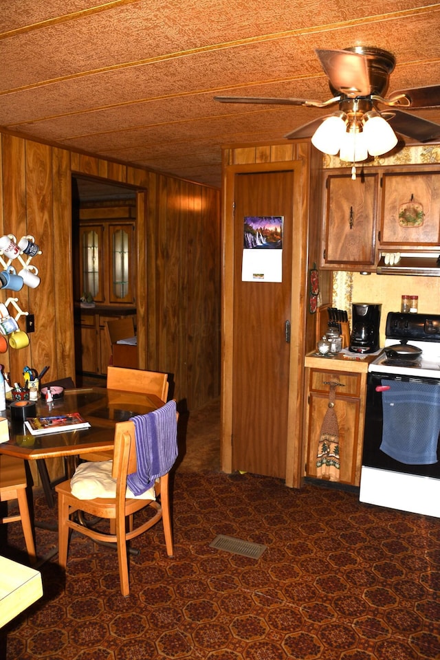 kitchen featuring visible vents, brown cabinets, white electric range, wood walls, and ceiling fan