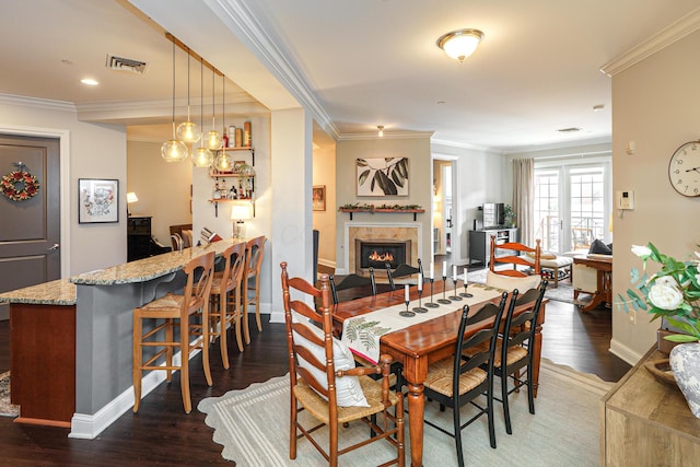 dining room with visible vents, wood finished floors, crown molding, and a tiled fireplace