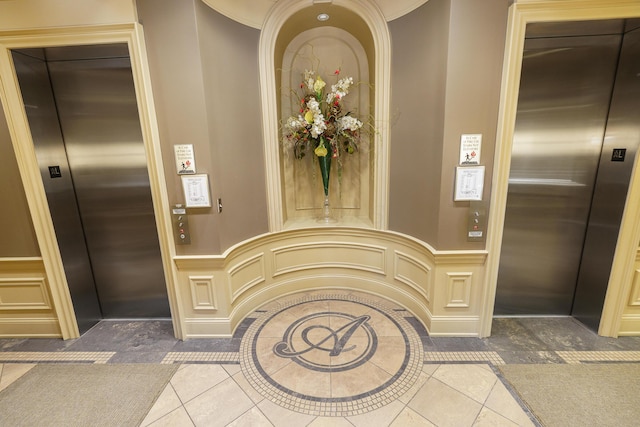 foyer featuring tile patterned flooring, elevator, wainscoting, and a decorative wall