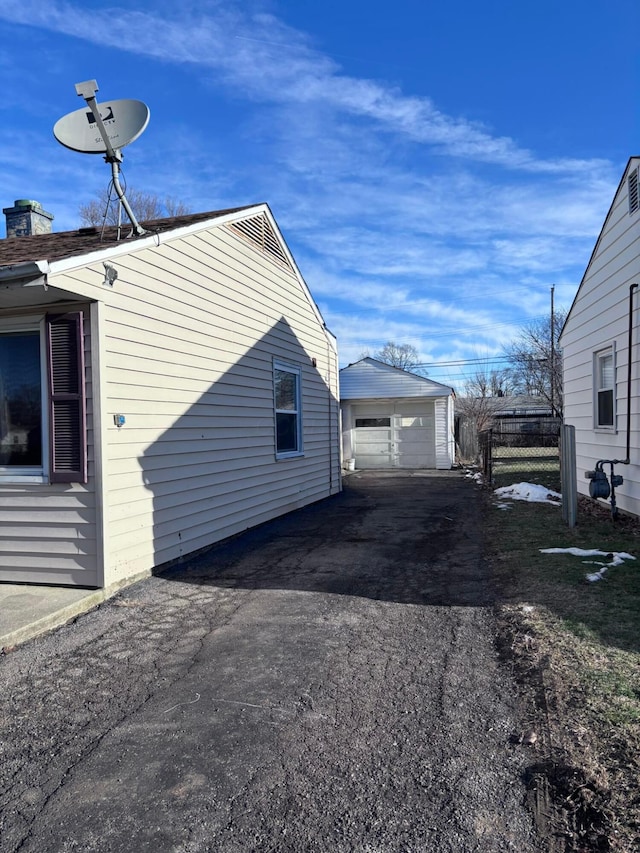 view of side of property with aphalt driveway, a garage, an outdoor structure, and fence