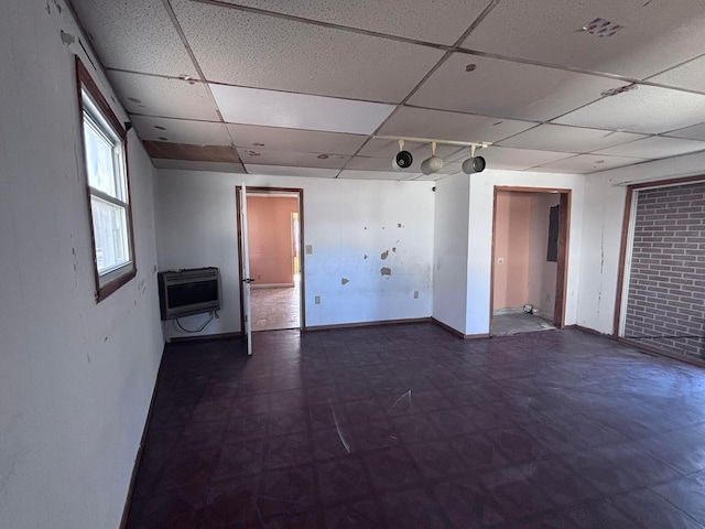 spare room with heating unit, a drop ceiling, tile patterned floors, and baseboards