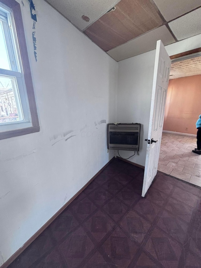 interior space featuring heating unit, baseboards, and a drop ceiling