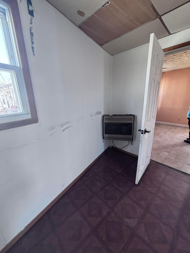 hallway with heating unit, a drop ceiling, and baseboards