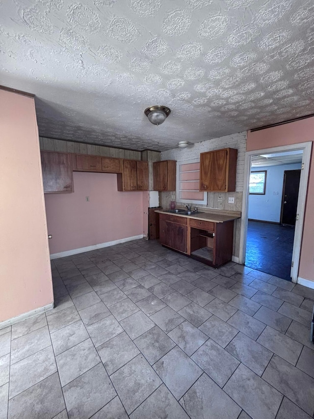 kitchen featuring brown cabinets, a sink, a textured ceiling, light countertops, and baseboards