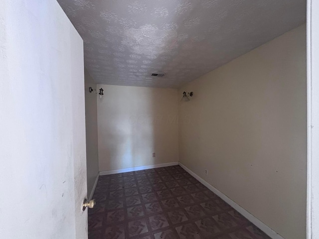 spare room featuring tile patterned floors, visible vents, baseboards, and a textured ceiling