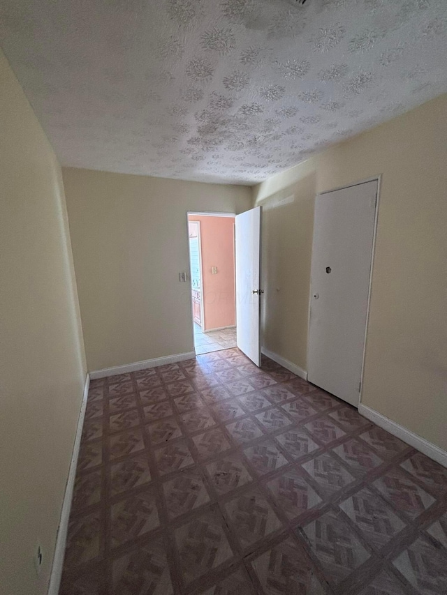 unfurnished room with baseboards and a textured ceiling