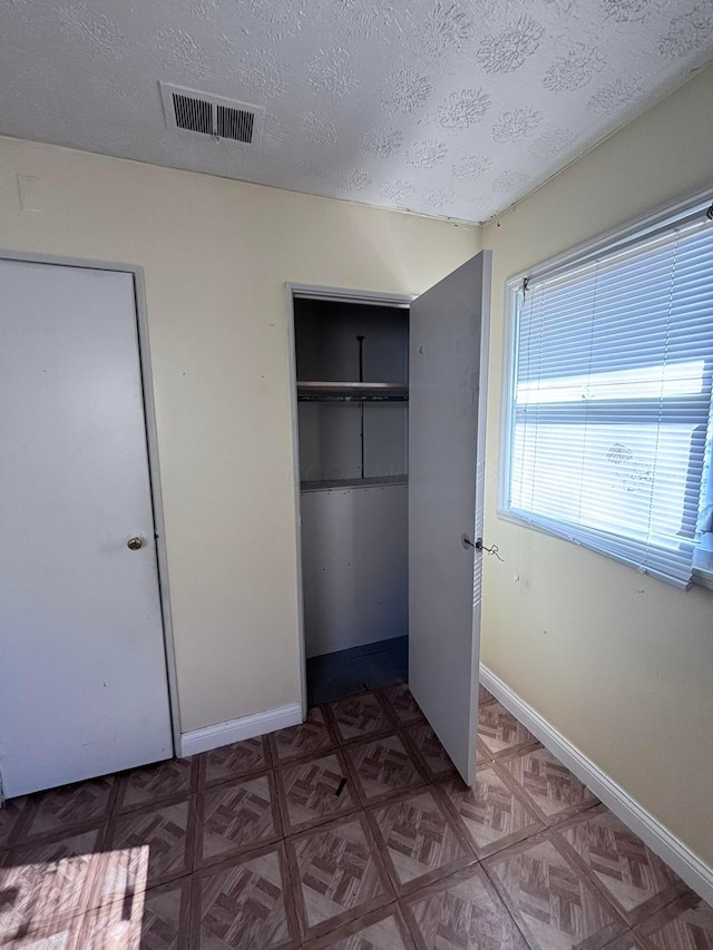 unfurnished bedroom featuring visible vents, baseboards, a textured ceiling, and a closet