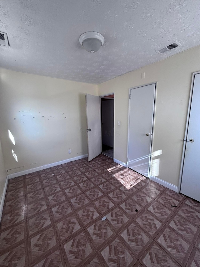 unfurnished bedroom featuring visible vents, a textured ceiling, and baseboards