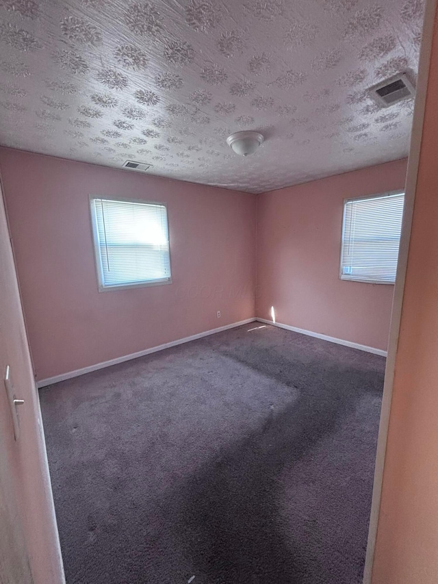 carpeted spare room with visible vents, baseboards, and a textured ceiling