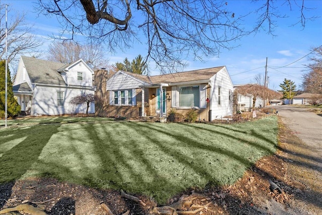 view of front of home featuring brick siding, a chimney, and a front yard