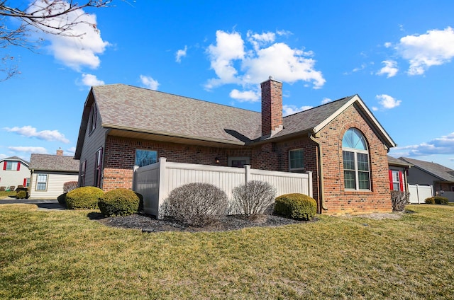 view of side of property with fence, a yard, roof with shingles, brick siding, and a chimney