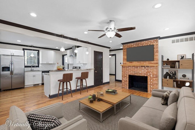 living area featuring visible vents, a brick fireplace, ornamental molding, and light wood finished floors