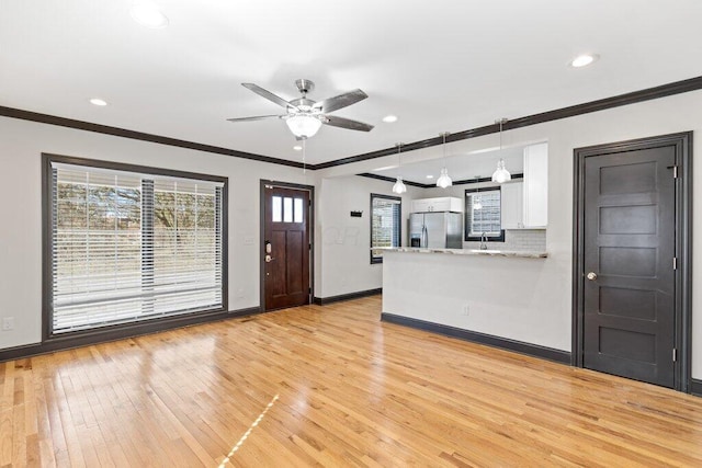 unfurnished living room featuring light wood finished floors, crown molding, baseboards, recessed lighting, and a sink