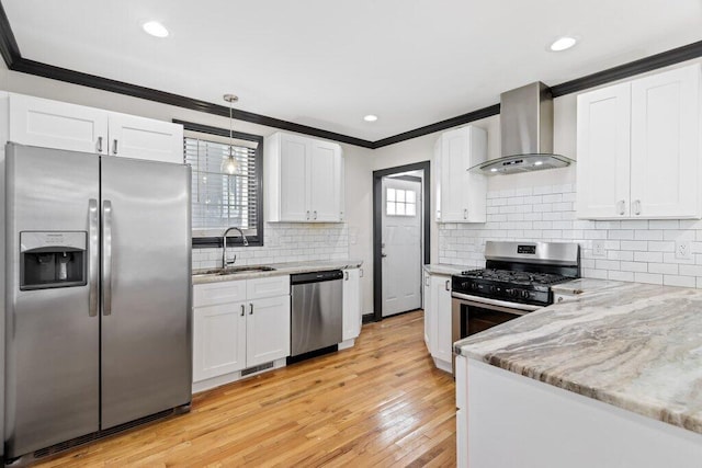 kitchen with ornamental molding, a sink, stainless steel appliances, white cabinets, and wall chimney range hood