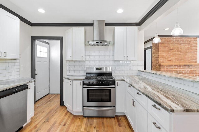 kitchen featuring wall chimney range hood, light wood-type flooring, ornamental molding, white cabinets, and stainless steel appliances