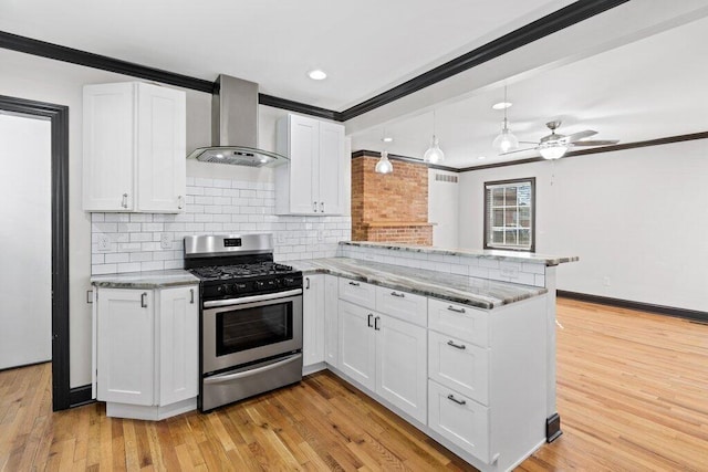 kitchen with a peninsula, white cabinets, crown molding, wall chimney range hood, and stainless steel gas range