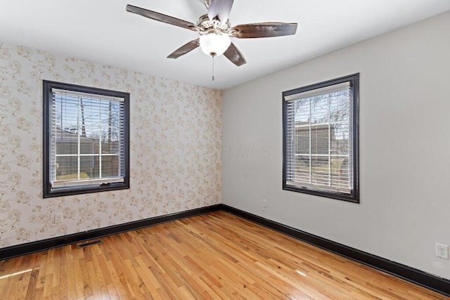 empty room with light wood-type flooring, visible vents, wallpapered walls, baseboards, and ceiling fan